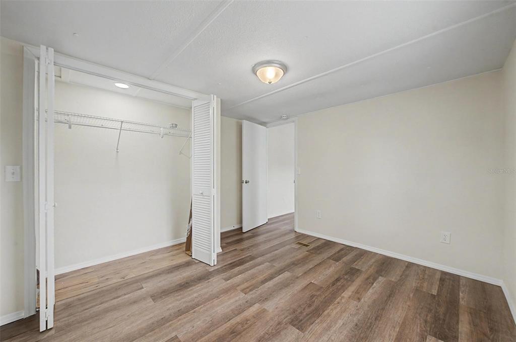 An empty bedroom features wood-look flooring, a white closet with louvered doors, and a ceiling light — 7338 FIRST LOOP AVENUE, BROOKSVILLE, FL