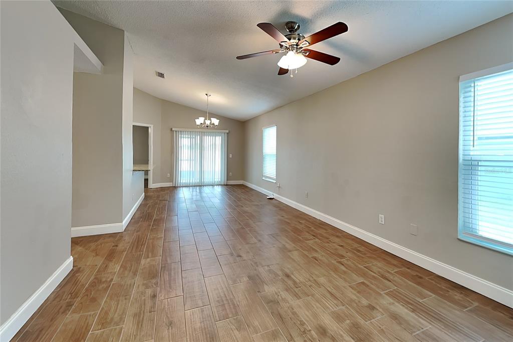 An empty living and dining area features wood-look tile flooring, beige walls, and vaulted ceilings — 310 DIAMOND RIDGE BOULEVARD, AUBURNDALE, FL