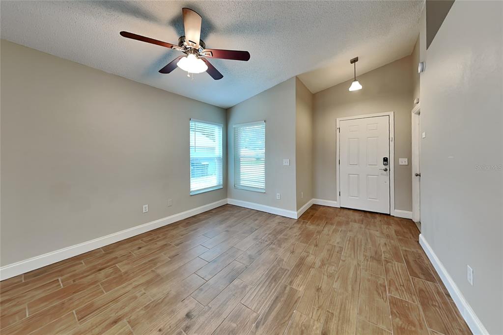 An empty room features wood-look tile flooring, a ceiling fan, and a white front door — 310 DIAMOND RIDGE BOULEVARD, AUBURNDALE, FL