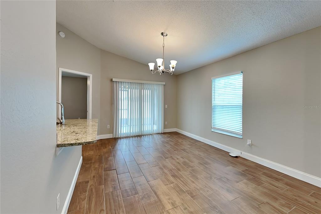 An empty dining room features wood-look tile flooring, a chandelier, and sliding glass patio doors — 310 DIAMOND RIDGE BOULEVARD, AUBURNDALE, FL