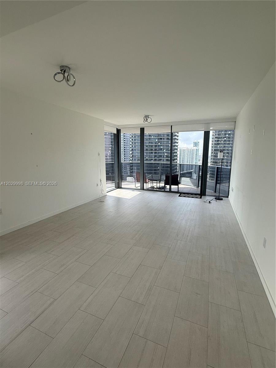 This living room features light wood-look tile flooring, white walls, and a balcony with city views — 1000 Brickell Plz # 3412, Miami FL 33131, MIAMI, FL