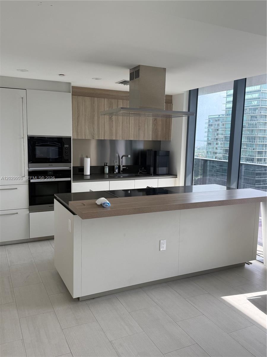 A modern kitchen features white cabinetry, wood-toned accents, a center island, and floor-to-ceiling windows — 1000 Brickell Plz # 3412, Miami FL 33131, MIAMI, FL