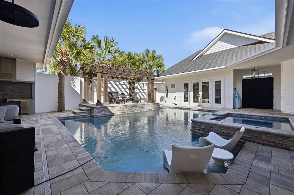 A backyard features a swimming pool with a spa, a wooden pergola, and patio furniture — 1026 SW 120TH DRIVE, GAINESVILLE, FL