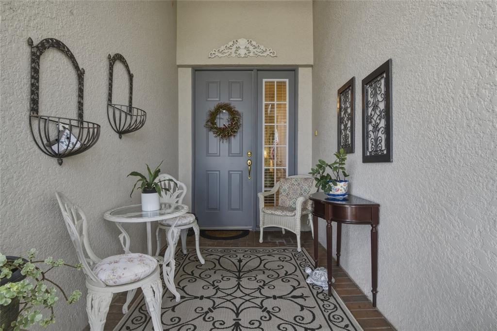 A covered entryway features a gray front door, patio furniture, and decorative wall hangings — 1066 MESA VERDE COURT, CLERMONT, FL