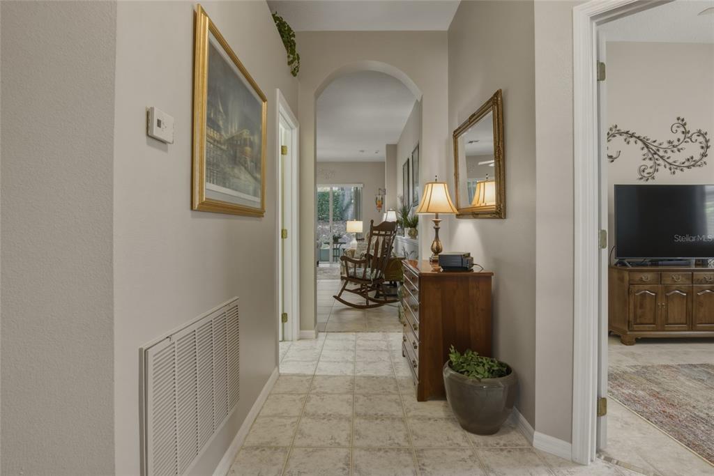 A tiled hallway leads through an arched doorway toward a living area with a rocking chair — 1066 MESA VERDE COURT, CLERMONT, FL