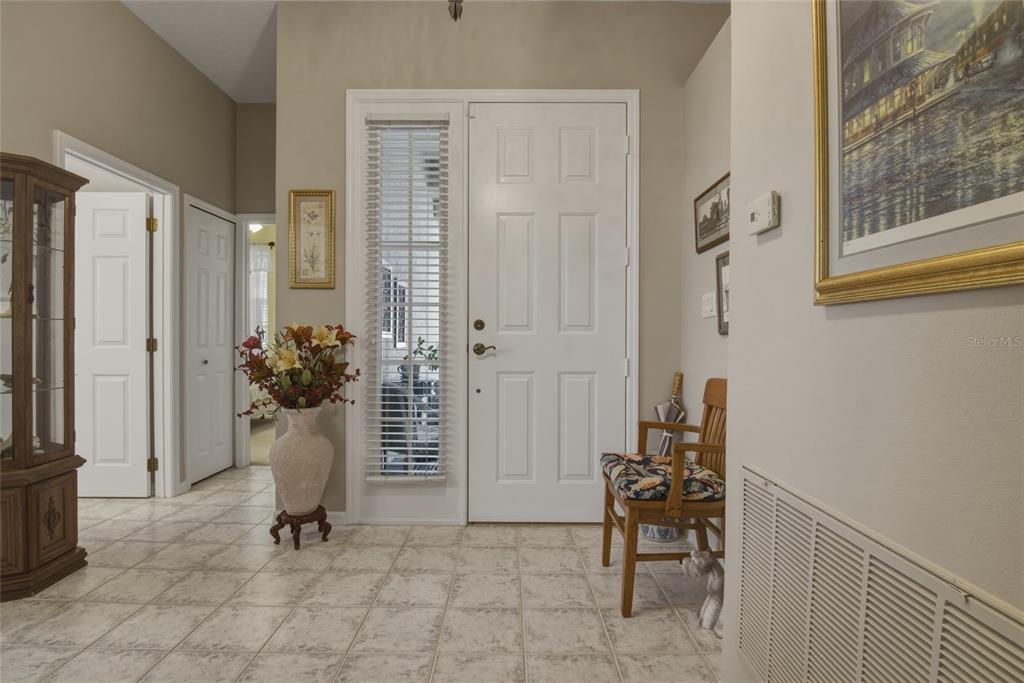 A tiled entryway features a white front door with a side window and a wooden chair — 1066 MESA VERDE COURT, CLERMONT, FL