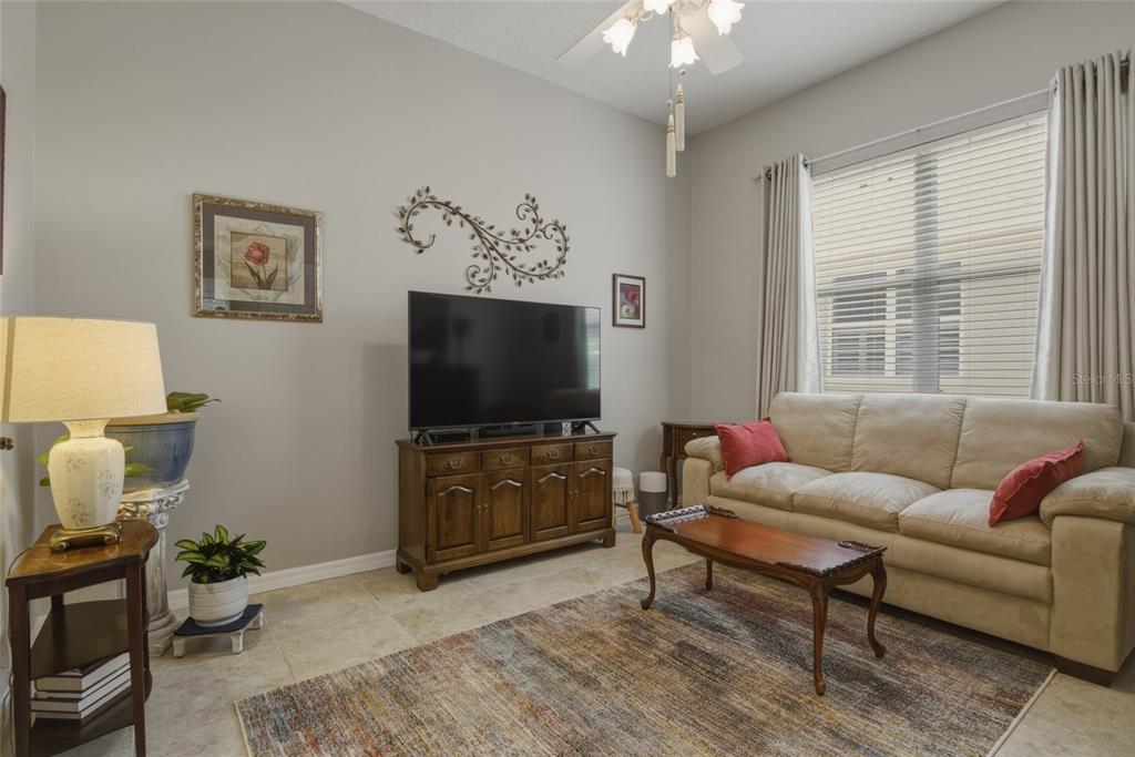 A living room features a beige sofa, a television on a wooden console, and tile flooring — 1066 MESA VERDE COURT, CLERMONT, FL