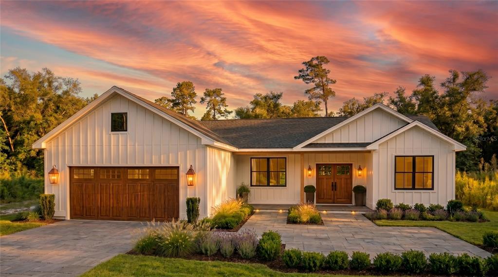 A white farmhouse-style home with a wooden garage door and double front doors at sunset — 35425 NUTMEG DRIVE, WEBSTER, FL