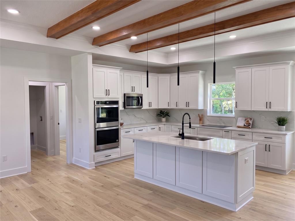 A modern white kitchen features a large island, stainless steel appliances, and exposed wood beams — 35425 NUTMEG DRIVE, WEBSTER, FL