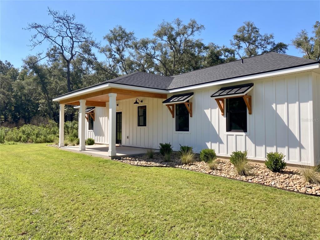 A white board-and-batten house exterior features a covered porch with wooden beams and black-framed windows — 35425 NUTMEG DRIVE, WEBSTER, FL