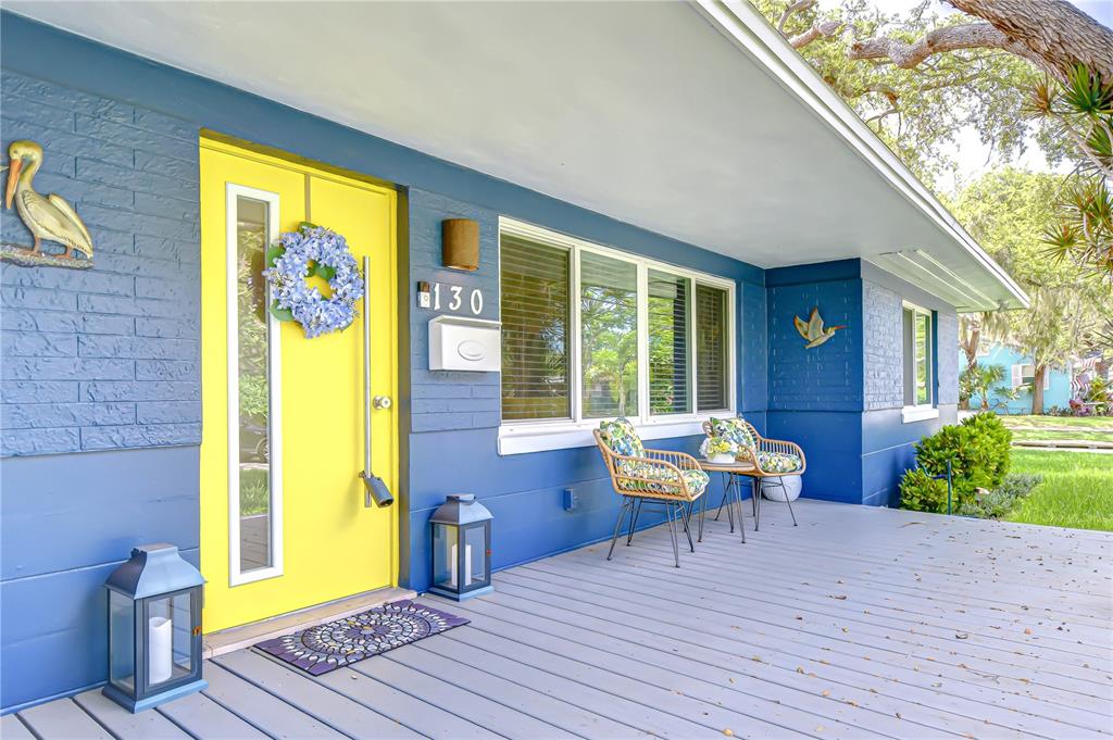 A blue house exterior features a bright yellow front door and a wooden porch — 130 63RD STREET S, ST PETERSBURG, FL