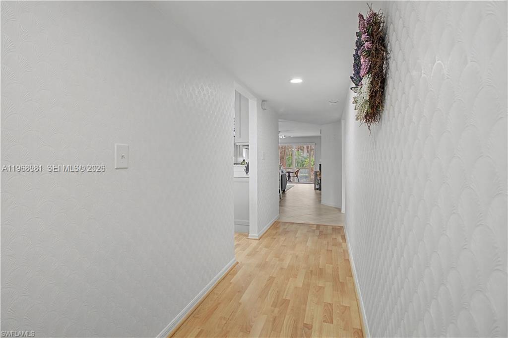 A hallway with textured white walls and light wood flooring leads toward an open living area — 741 Landover Cir # 102, Naples FL 34104, NAPLES, FL
