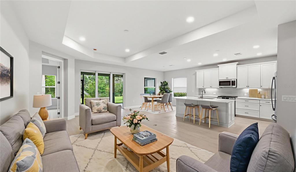 An open-concept living room and kitchen featuring light wood floors and white cabinetry — 3075 HERITAGE PINES DRIVE, FORT MYERS, FL