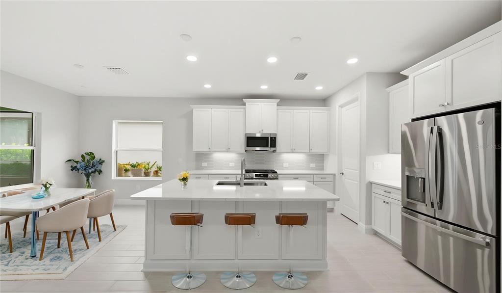 A modern white kitchen features a large center island with bar stools and stainless appliances — 3075 HERITAGE PINES DRIVE, FORT MYERS, FL