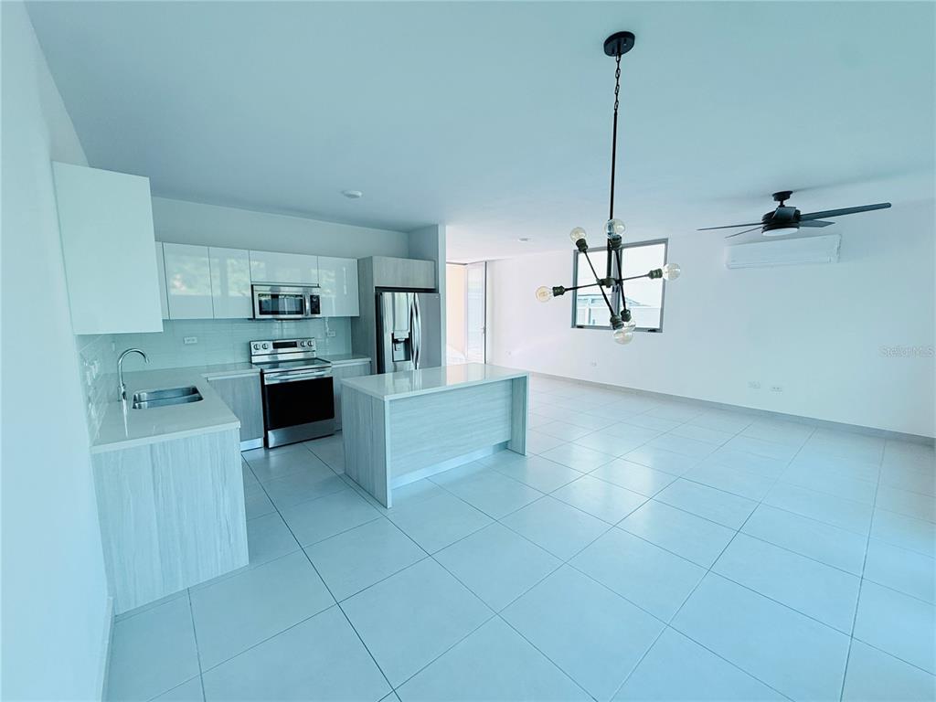 A modern kitchen features white cabinetry, stainless steel appliances, a center island, and tile flooring — Urb Riviera Court 57, BAYAMON, PR
