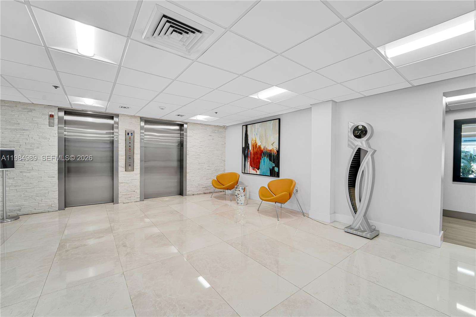 An elevator lobby features two stainless steel doors, white tiled walls, and two orange chairs — 919 Hillcrest Dr # 210, Hollywood FL 33021, HOLLYWOOD, FL