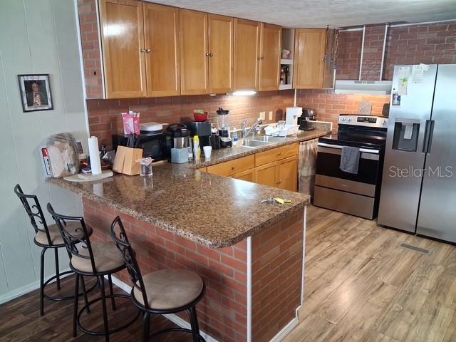 A kitchen features wood cabinets, a brick-faced breakfast bar, granite countertops, and stainless steel appliances — 5148 DARLINGTON ROAD, HOLIDAY, FL