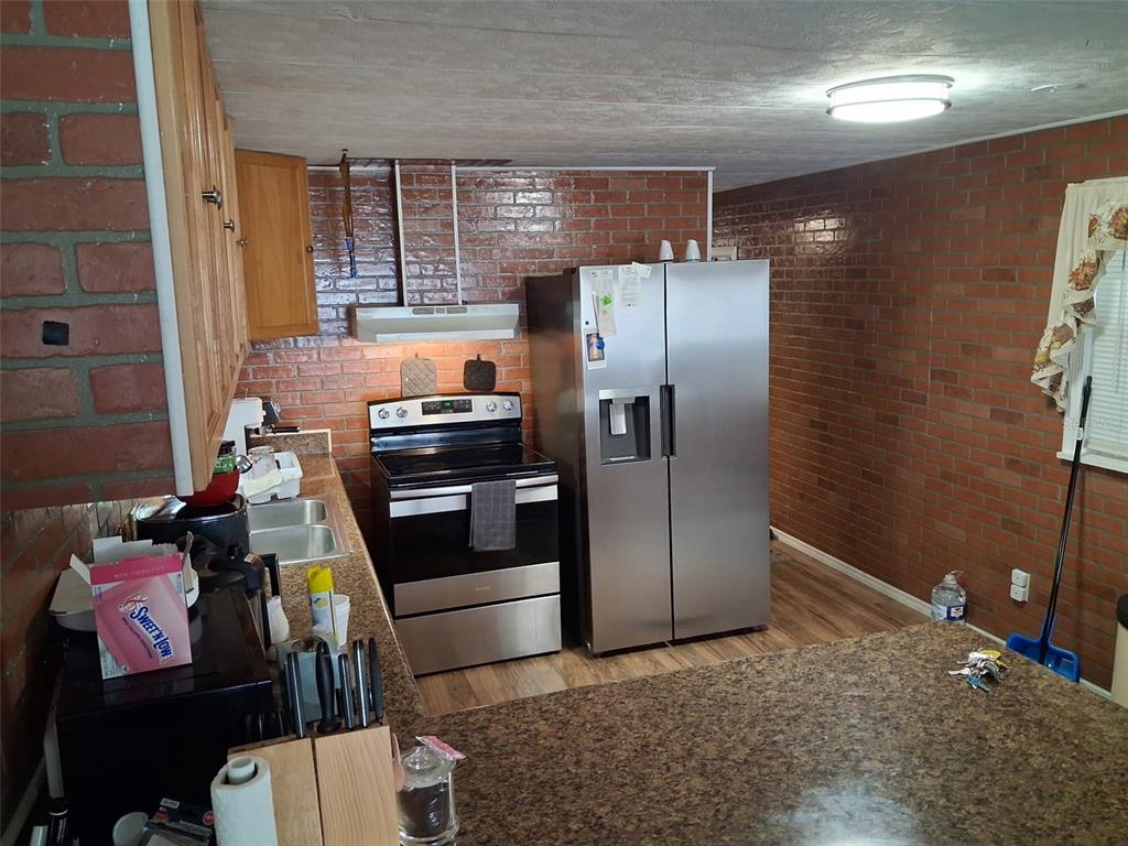 A kitchen features brick walls, stainless steel appliances, wood cabinets, and a granite-look countertop — 5148 DARLINGTON ROAD, HOLIDAY, FL