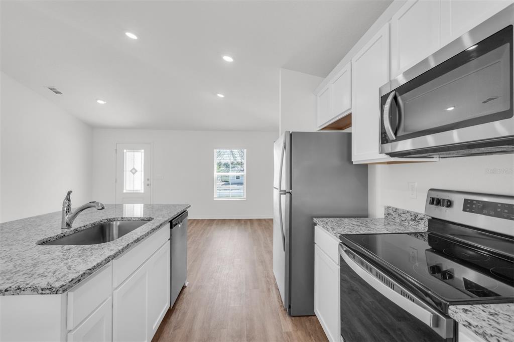 A kitchen with white cabinets, granite countertops, and stainless steel appliances overlooks an open living area — 2517 SW 165TH STREET ROAD, OCALA, FL
