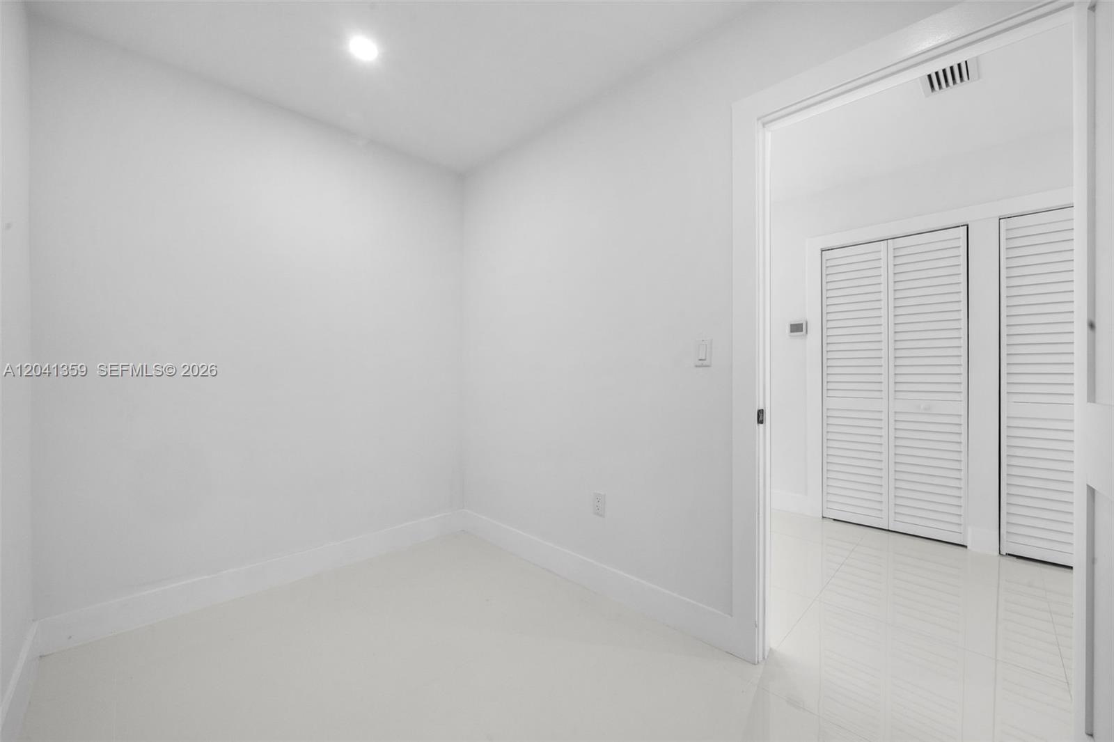 A small, empty room with white walls and tile flooring leads into a closeted hallway — 2940 SW 12th St, Miami FL 33135, MIAMI, FL