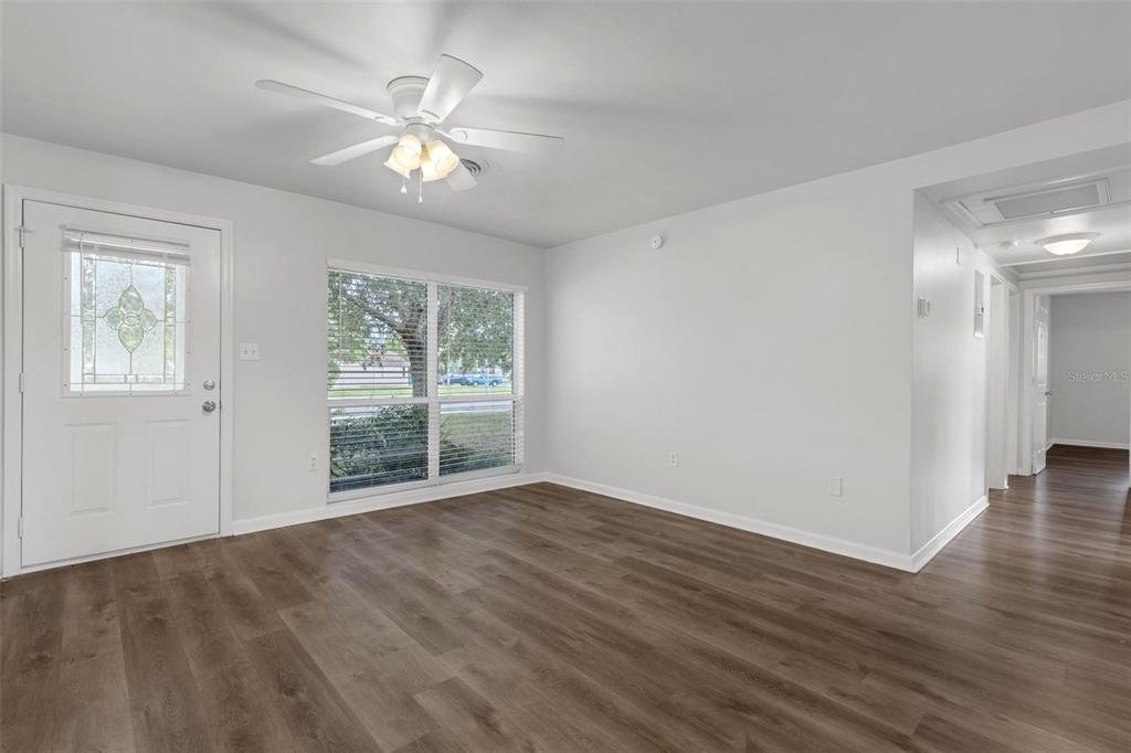 An empty room with white walls, wood-look flooring, a ceiling fan, and a front door — 203 E LAKEVIEW AVENUE, EUSTIS, FL