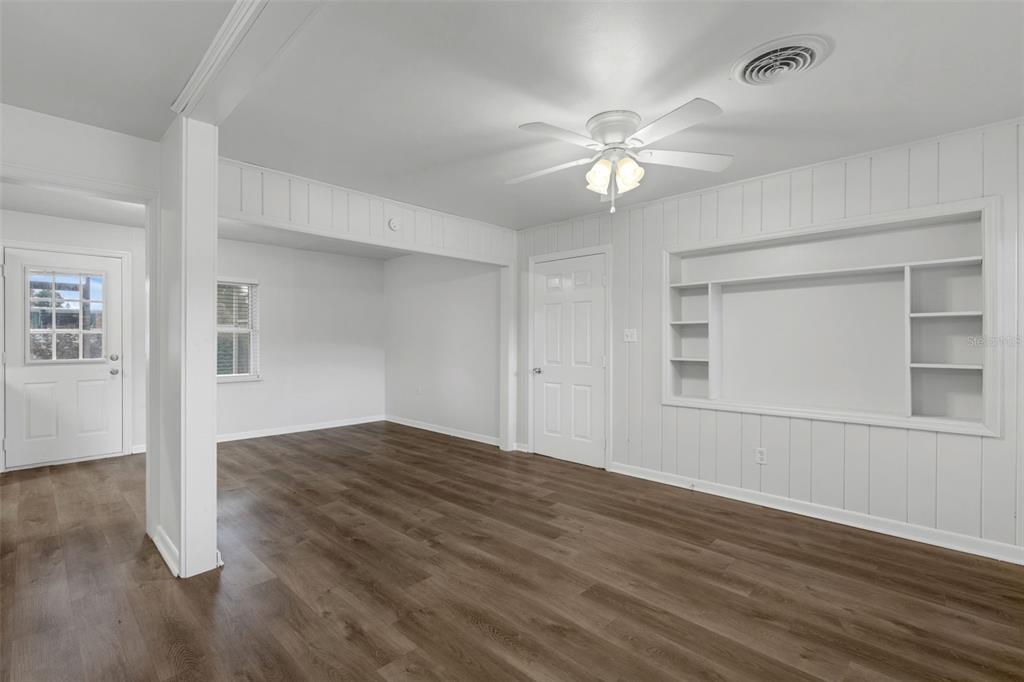 A bright room features white paneled walls, dark wood-look flooring, a ceiling fan, and built-in shelving — 203 E LAKEVIEW AVENUE, EUSTIS, FL