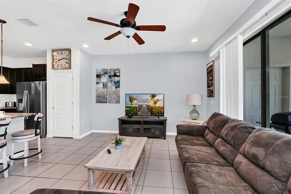 A living room features tile flooring, a dark sectional sofa, a television, and sliding glass doors — 8930 SYDNEY AVENUE, KISSIMMEE, FL