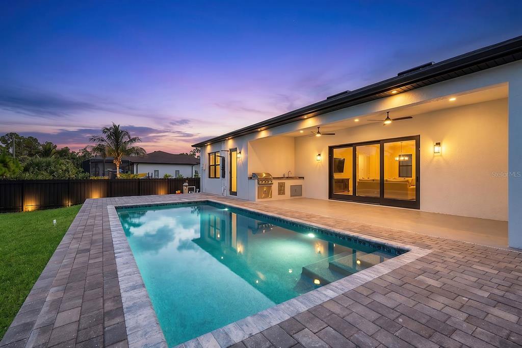 A backyard swimming pool with a paved deck and an outdoor kitchen under a covered patio — 15029 ACORN CIRCLE, PORT CHARLOTTE, FL