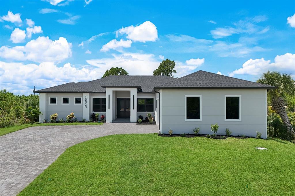 A modern, single-story house with a gray exterior, dark roof, and a paved driveway — 15029 ACORN CIRCLE, PORT CHARLOTTE, FL