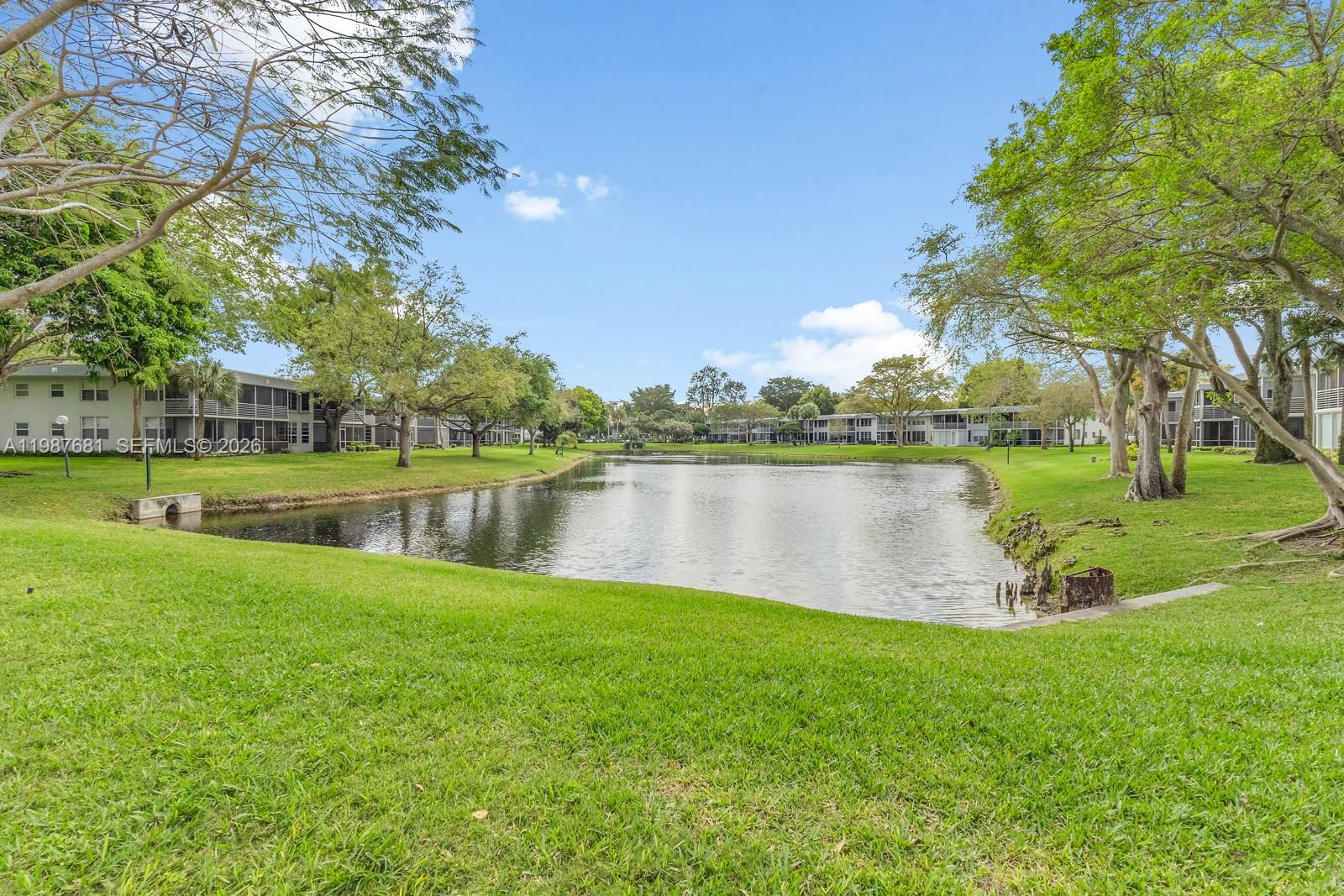 A grassy lawn slopes down to a pond surrounded by apartment buildings and trees — 4280 Oaks Ter # 102, Pompano Beach FL 33069, POMPANO BEACH, FL