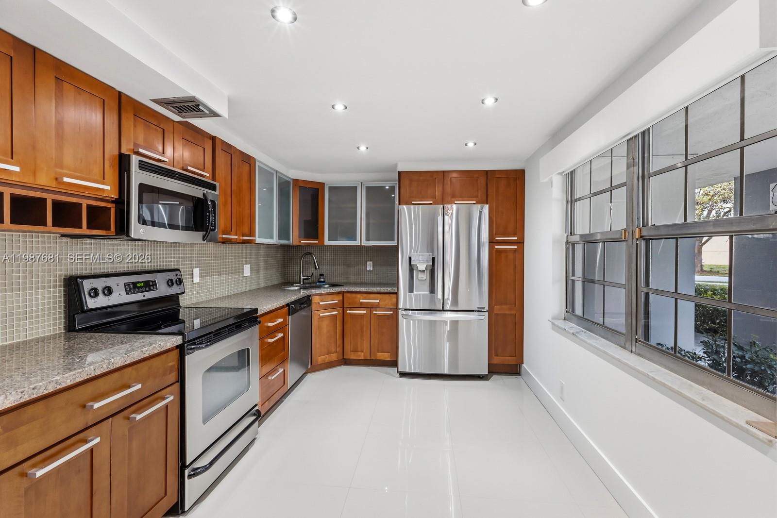 A kitchen features wood cabinets, stainless steel appliances, granite countertops, and white tile flooring — 4280 Oaks Ter # 102, Pompano Beach FL 33069, POMPANO BEACH, FL