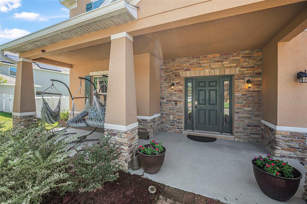 A covered front porch features stone veneer accents, a dark door, and two hanging chairs — 120 LOS ARBOR DRIVE, DELAND, FL