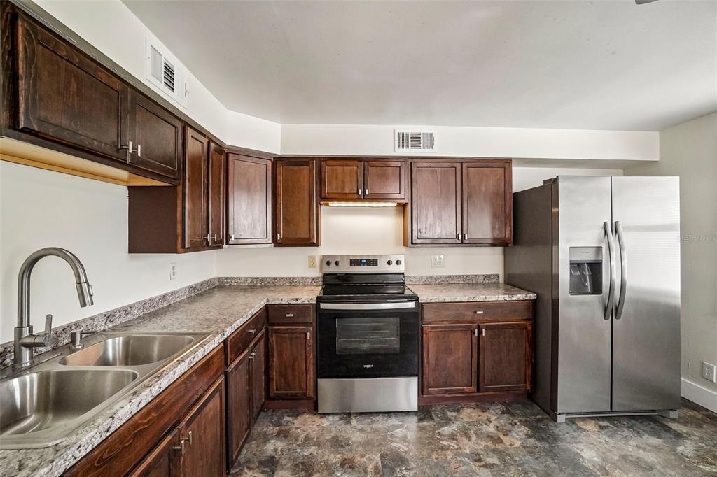 A kitchen features dark wood cabinets, granite-look countertops, stainless steel appliances, and a double sink — 9216 W ROBSON STREET, TAMPA, FL