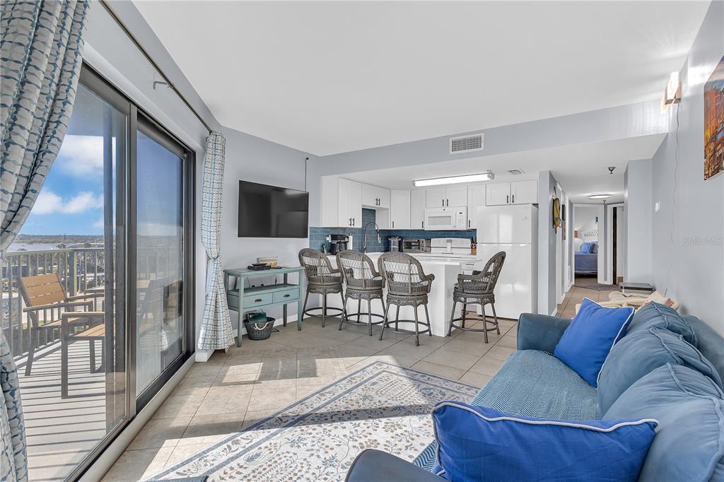 An open-concept living room and kitchen with tile floors, a blue sofa, and balcony access — 3647 S ATLANTIC AVENUE UNIT 407, DAYTONA BEACH, FL