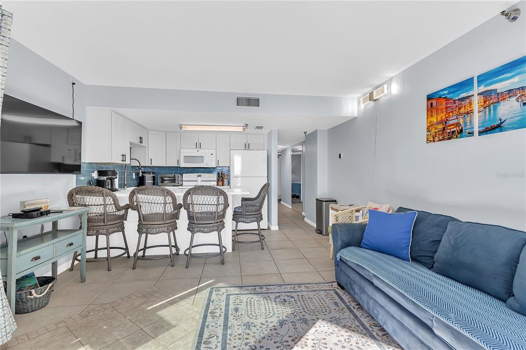 An open-concept living room and kitchen featuring tile floors, white cabinets, and a blue sofa — 3647 S ATLANTIC AVENUE UNIT 407, DAYTONA BEACH, FL