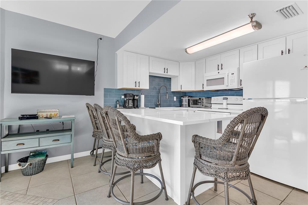A kitchen features white cabinetry, a blue tile backsplash, a white island, and wicker barstools — 3647 S ATLANTIC AVENUE UNIT 407, DAYTONA BEACH, FL