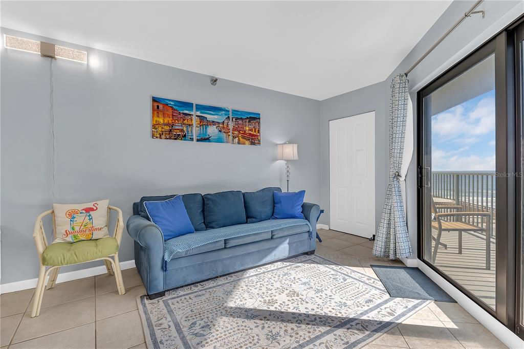 A living room features a blue sofa, a patterned rug, and a sliding glass door — 3647 S ATLANTIC AVENUE UNIT 407, DAYTONA BEACH, FL