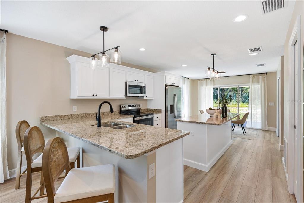 A kitchen features white cabinets, granite countertops, a central island, and light wood-look flooring — 515 E ANDERSON AVENUE, BUSHNELL, FL