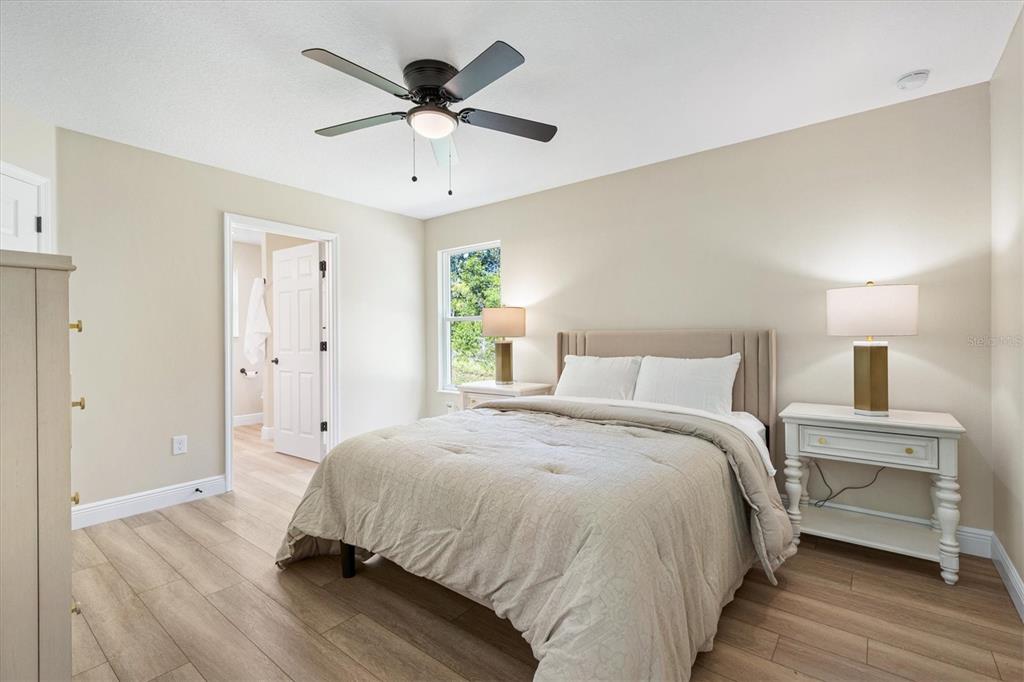 A bedroom features light wood-look flooring, a ceiling fan, and a bed with two nightstands — 515 E ANDERSON AVENUE, BUSHNELL, FL