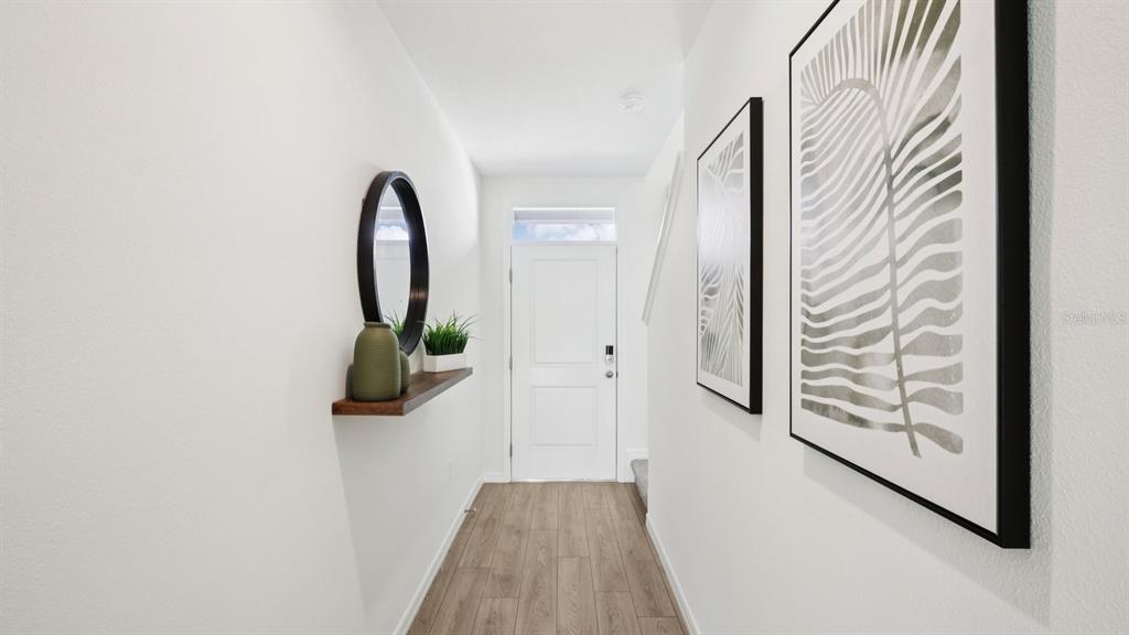 A bright entryway features wood-look flooring, a floating shelf with decor, and framed wall art — 31185 MIDNIGHT SUN WAY, WESLEY CHAPEL, FL