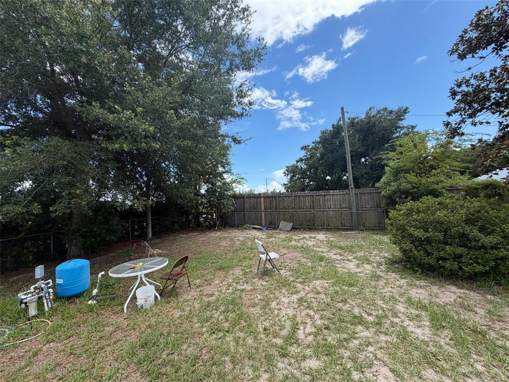 A backyard features a wooden fence, scattered patio furniture, and a blue water tank — 1724 S US 301, SUMTERVILLE, FL