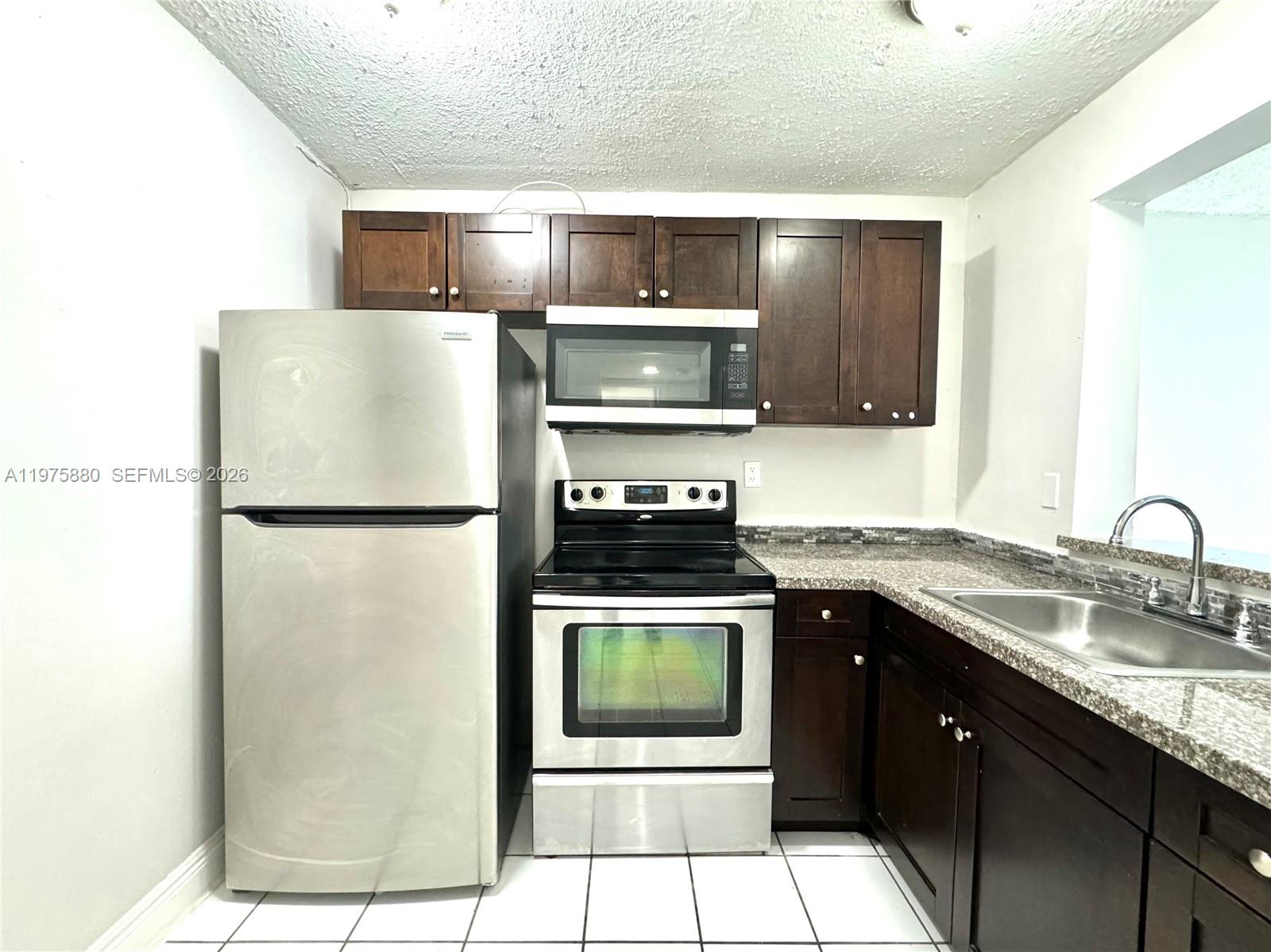 A kitchen features dark wood cabinets, stainless steel appliances, and granite countertops over tiled floors — 484 NW 165th St Rd # 411, Miami FL 33169, MIAMI, FL