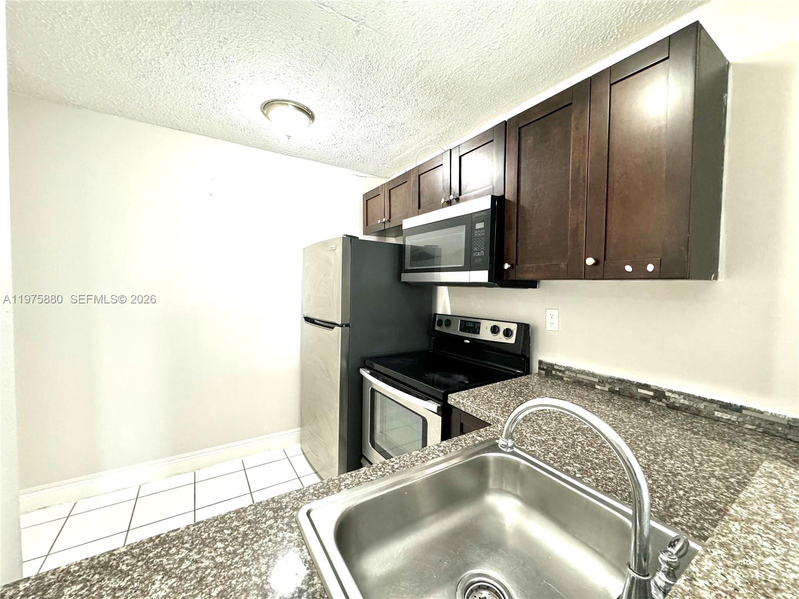A kitchen features dark wood cabinets, stainless steel appliances, and granite countertops — 484 NW 165th St Rd # 411, Miami FL 33169, MIAMI, FL
