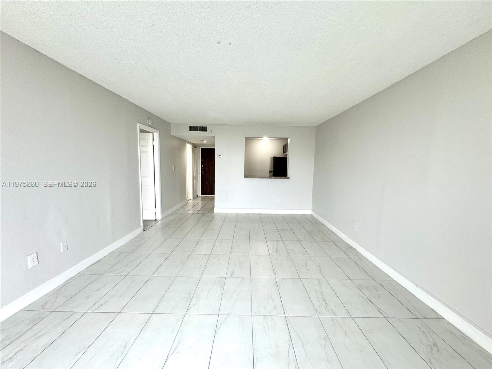 An empty living area features light gray walls, white tile flooring, and a kitchen pass-through — 484 NW 165th St Rd # 411, Miami FL 33169, MIAMI, FL
