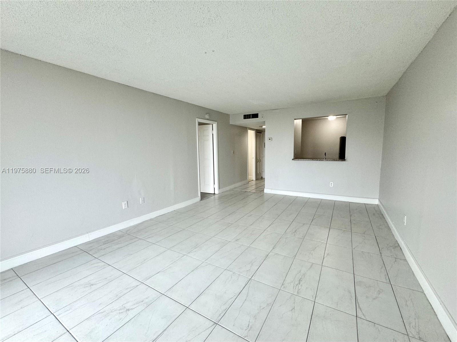 An empty room features light gray walls, white tile flooring, and a kitchen pass-through window — 484 NW 165th St Rd # 411, Miami FL 33169, MIAMI, FL