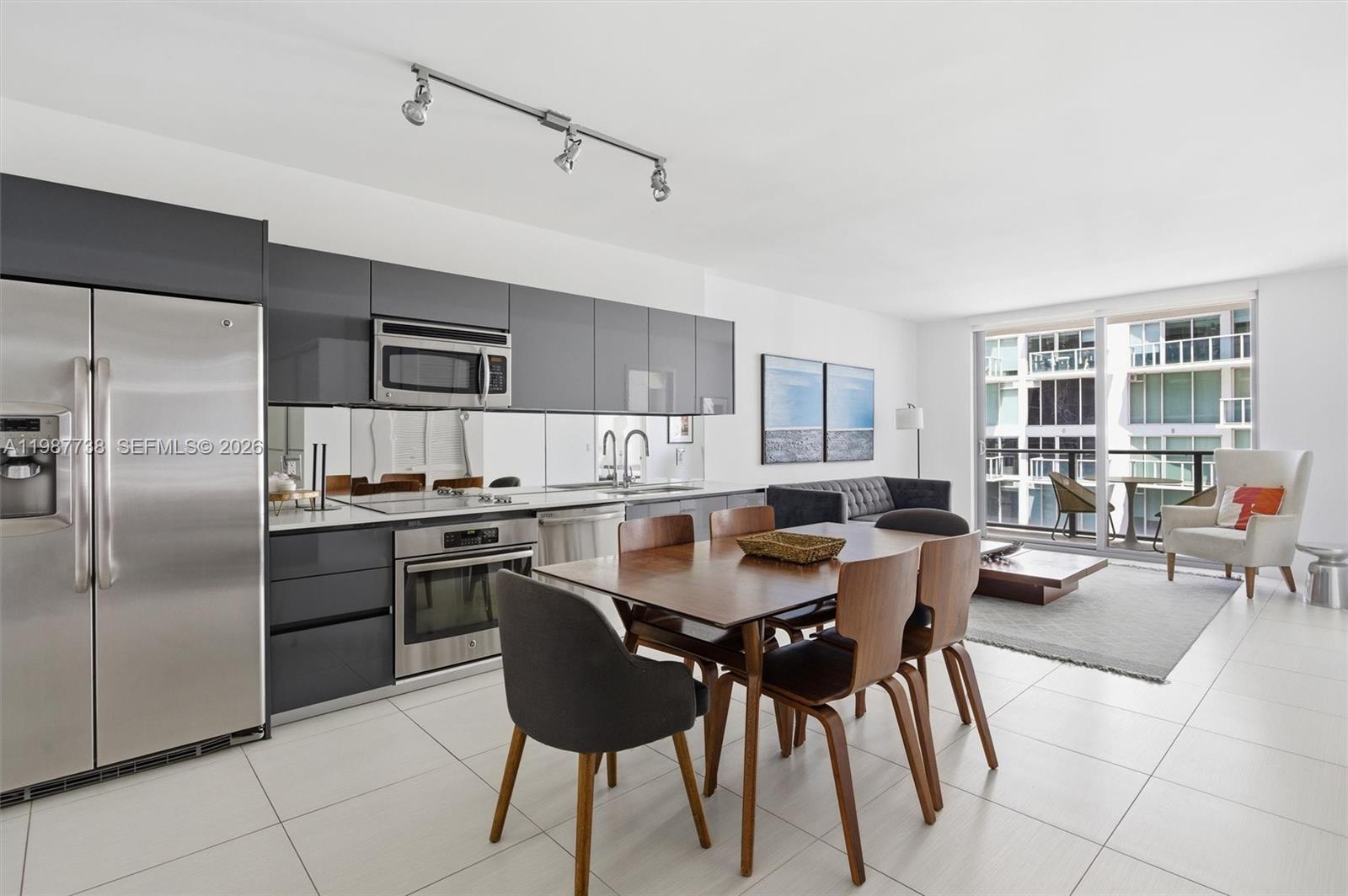 A modern open-concept kitchen and dining area features gray cabinetry, stainless steel appliances, and tile flooring — 31 SE 6th St # 2504, Miami FL 33131, MIAMI, FL