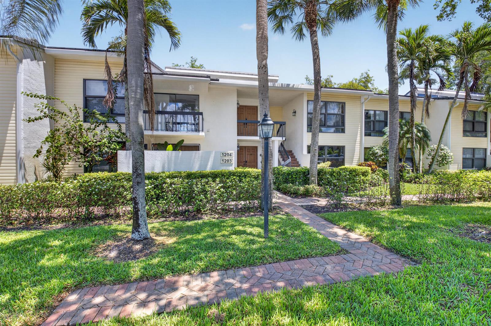 A two-story apartment building with beige siding, palm trees, and a brick walkway — 6760 Willow Wood Drive # 1204, Boca Raton FL 33434, BOCA RATON, FL