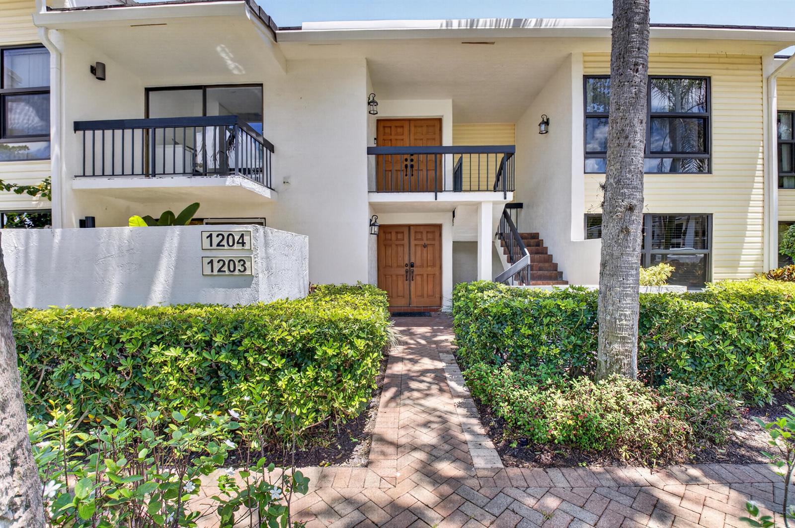 A two-story residential building with a brick walkway, wooden double doors, and manicured hedges — 6760 Willow Wood Drive # 1204, Boca Raton FL 33434, BOCA RATON, FL