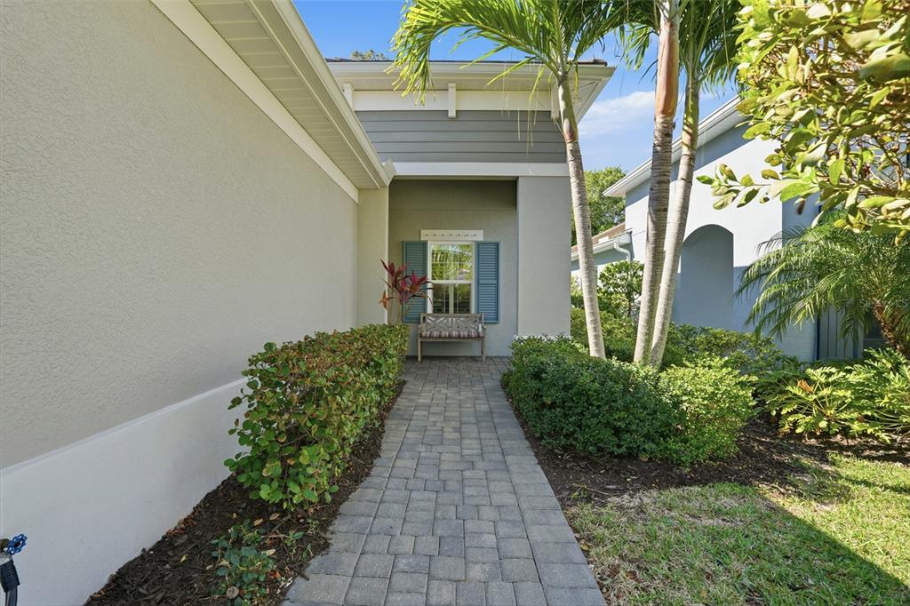 A paved walkway leads to a covered entryway with a bench and blue shutters — 11655 SOLANO DRIVE, FORT MYERS, FL