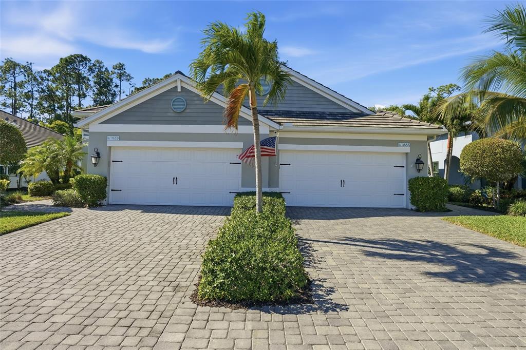 A two-car garage duplex with a paved driveway, a central palm tree, and landscaping — 11655 SOLANO DRIVE, FORT MYERS, FL